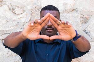 African American guy demonstrating triangle gesture with hands near fence photo