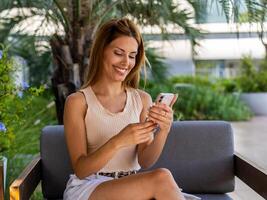 Smiling woman is sitting on a sofa while she turns off her smartphone photo