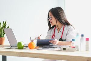 Asian doctor with documents browsing laptop in hospital photo