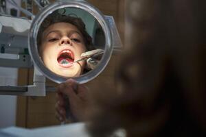 Dentist checking boy using mouth mirror in office photo
