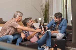 Father and mature sons clinking beer bottles and smiling at home photo