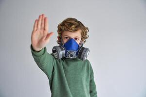 Calm child in respirator showing keep distance gesture in gray s photo