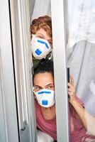 Mother with son in protective masks looking out window photo