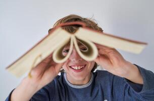 Cheerful boy looking at camera through opened book photo