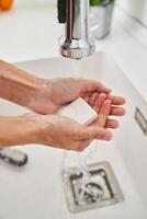 Person washing hands with soap under water in sink photo