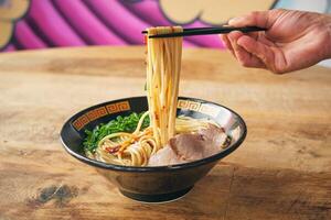Crop person with noodles on chopsticks above delicious ramen photo