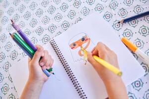 Crop kid drawing picture in notepad at table photo