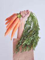 Crop female hand reached out from packet with carrots photo