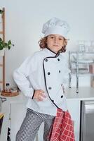 Confident boy in cook uniform in kitchen photo