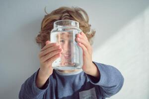 Smiling boy looking through glass jar photo