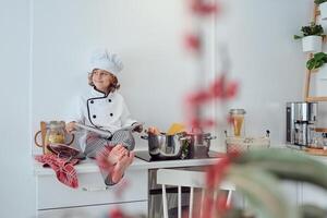 Dreamy preteen boy in chef uniform sitting scrolling cookbook photo