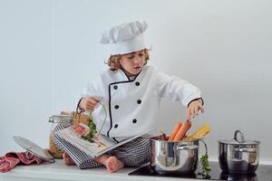 Positive boy sitting on counter and putting vegetables into sauc photo