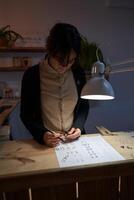 Focused female jeweler with ring and sketches at table photo