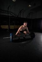 Young strong sportsman doing exercises with barbell with weights photo