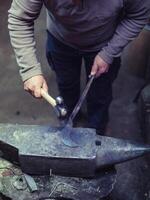 Crop anonymous master using hammer while forging metal on anvil photo