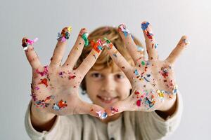 Smiling boy showing palms with stuck colorful confetti photo