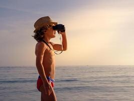 Boy enjoying seascape through binoculars at sunset photo