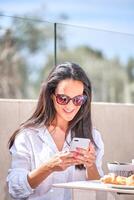 Smiling woman messaging on smartphone while having breakfast in photo