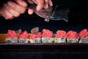 Faceless chef slicing truffle on sushi rolls with tuna photo