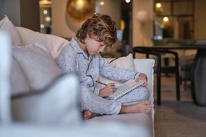 Boy in pajama drawing in sketchbook at home photo