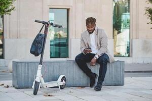 Ethnic man sitting on bench in street with smartphone in shade o photo