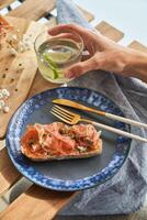 Anonymous person having breakfast with prosciutto toast and lime water on terrace photo
