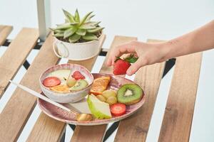 Unrecognizable person taking strawberry from plate with yogurt and fruits photo