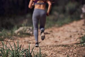 Crop faceless female jogger running on pathway in woods photo