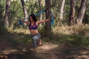 Fit ethnic lady squatting and outstretching arms with resistance photo