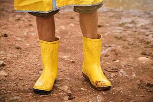 Crop child wearing yellow raincoat and standing in mud photo