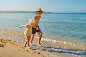 Happy smiling boy holding hand of little girl on beach and runni photo