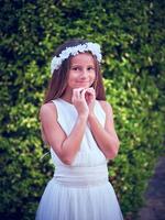 Smiling girl in flower wreath standing against green trees photo