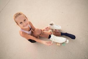 Smiling girl putting on roller skates and looking at camera photo