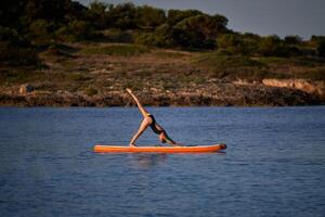 Sportswoman taking Downward Facing Dog pose on paddleboard in se photo