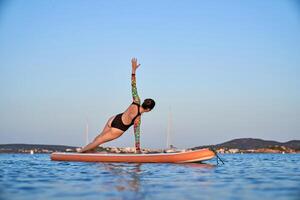 Unrecognizable woman practicing yoga in Side Plank on paddleboar photo