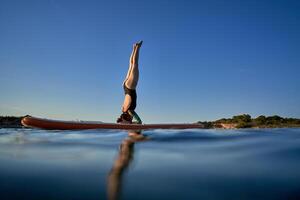 Unrecognizable woman practicing Supported Headstand on SUP board photo