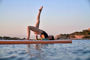 Fit woman taking bridge pose on paddleboard photo