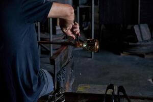 Crop man making glass using rod and tongs in workshop photo