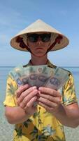 Man in Vietnamese hat counting Vietnamese Dong bills on exotic beach in Vietnam video