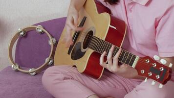Closeup of an unidentified woman guitarist plucking strings of six string acoustic guitar in process of learning, developing technique and musical style during musical education. Handheld, zoom in video