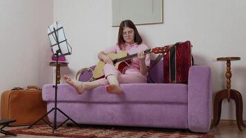 Woman depicted playing guitar, showcasing refined technique that attests to proficiency in art of music. She engaged in refinement of musical abilities within confines of personal studio. Zoom in video