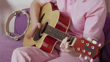 Closeup unidentified woman's hands strumming strings of acoustic guitar. She appears to be musician who is still learning and developing technique and style during musical training. Handheld, zoom in video