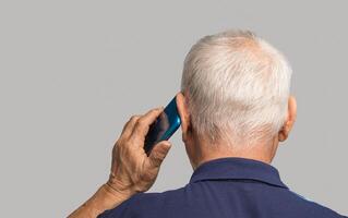 Back view of a senior man using a smartphone while standing on a gray background. photo