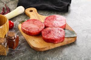 Three raw beef steaks on a cutting board next to spices and other ingredients photo