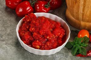 A bowl of tomato sauce next to a bowl of tomatoes photo