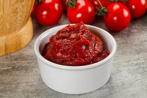 A bowl of tomato sauce next to a wooden chopping board photo