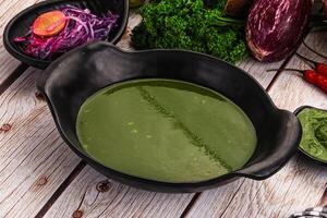 A bowl of green soup on a table next to a bowl of vegetables photo