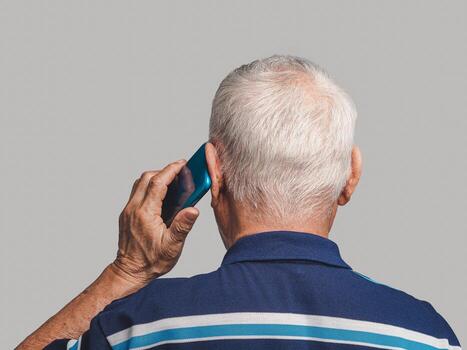 Back view of a senior man using a smartphone while standing on a gray background photo