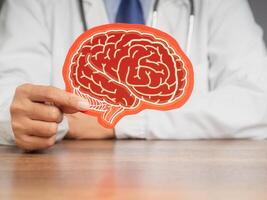 Doctor in a uniform holding a brain symbol made from red paper while sitting at the table. Close-up photo