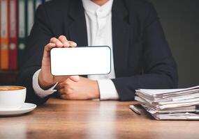 Businessman holding a white blank screen smartphone while sitting at the table. Space for text. photo